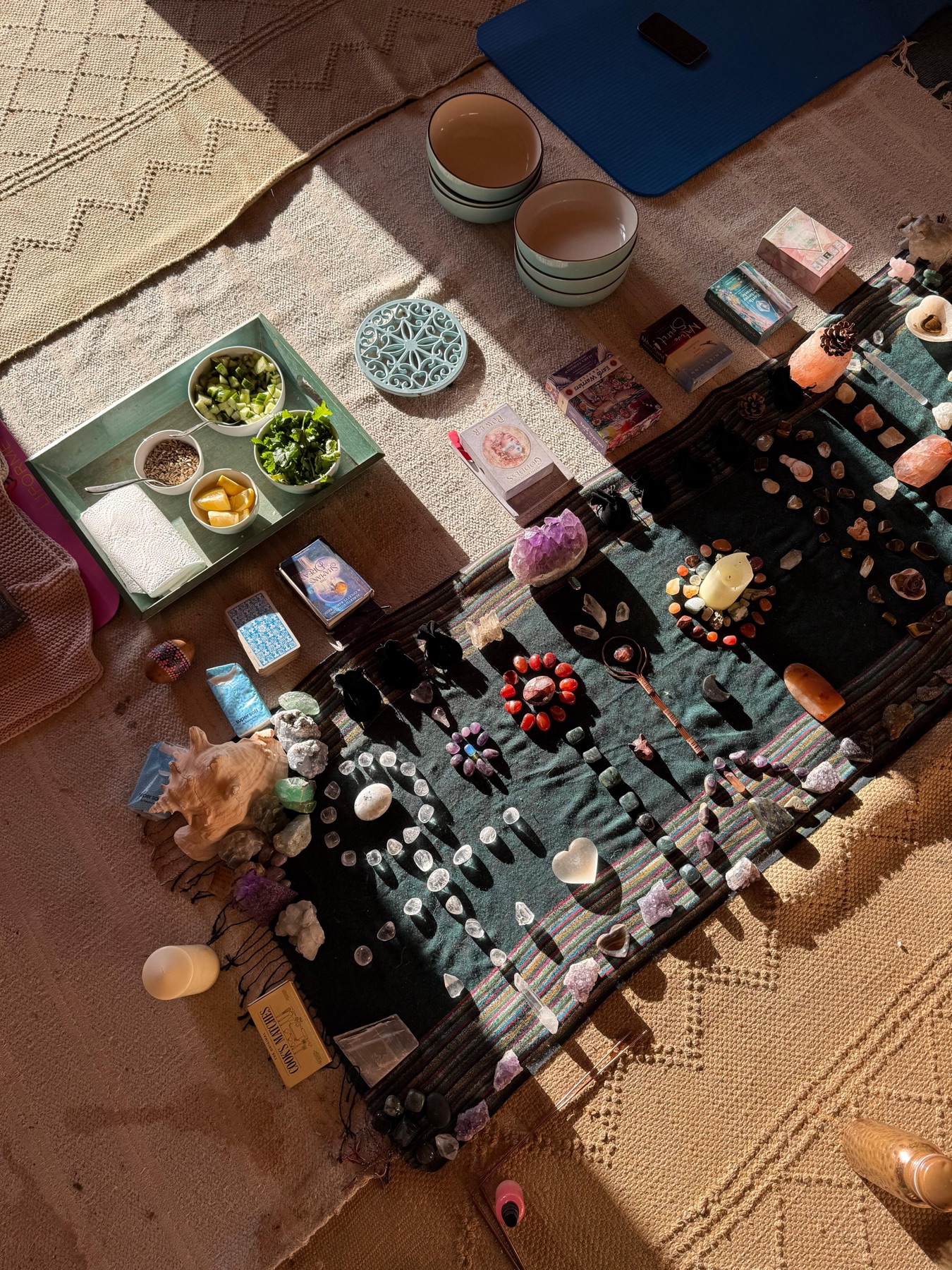 A ceremony altar laid out on a woven rug: crystals, cacao bowls, cards and candles