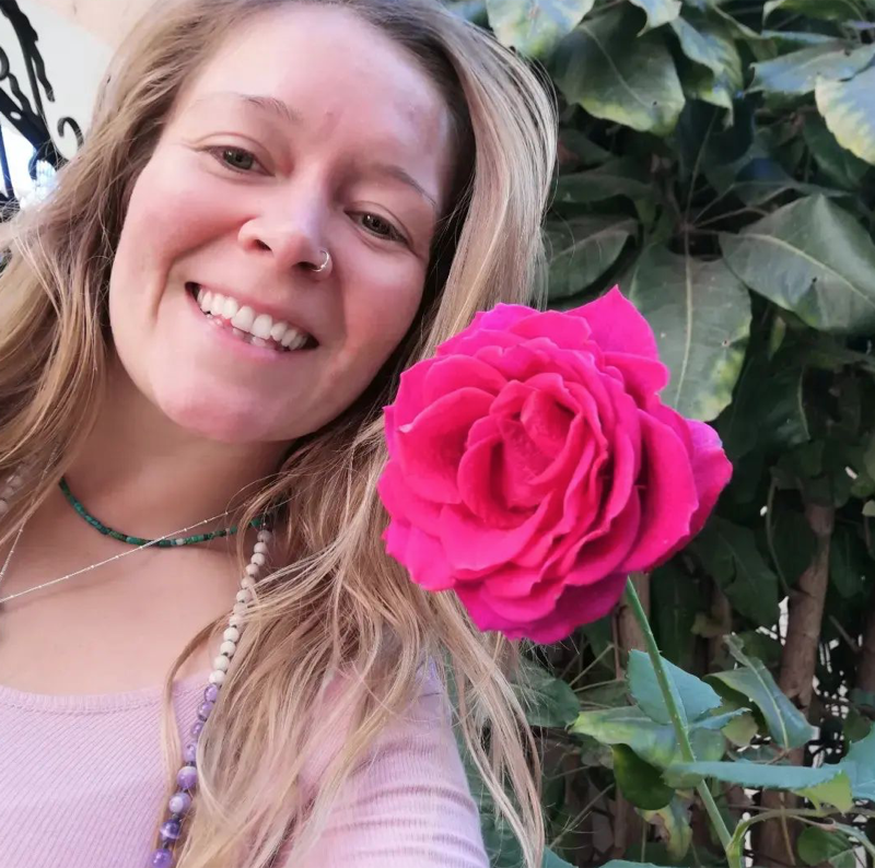 Jade smiling beside a deep pink rose